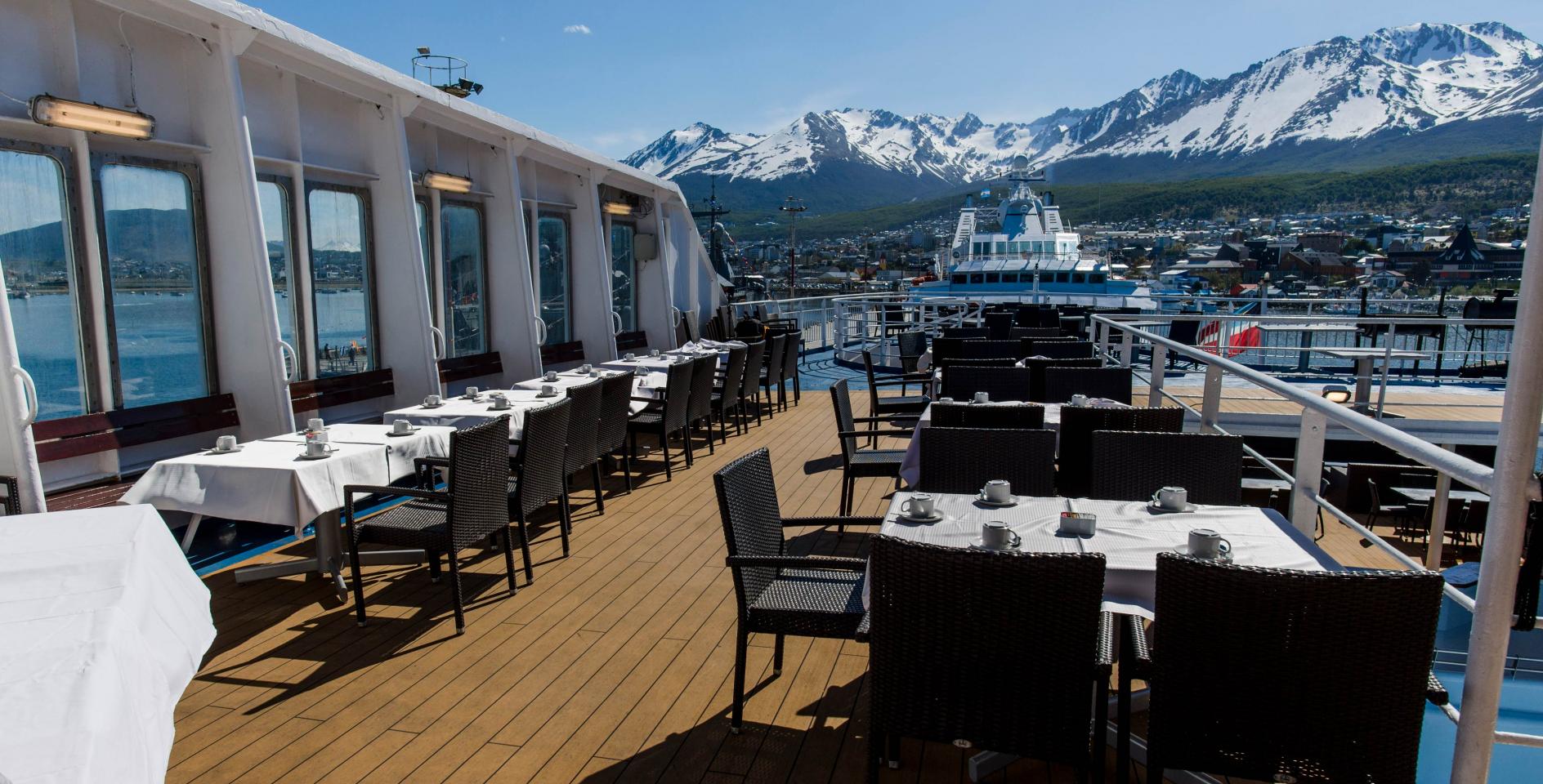 Outdoor dining area on upper deck of Ocean Endeavour, with view of snow-capped mountains beyond